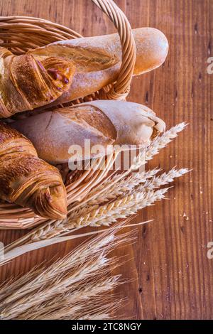 Close up view on baguettes and croissants in wicker basket with ears of wheat on old wooden boards Stock Photo