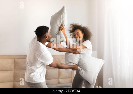 Joyful African Couple Having Pillow Fight For Fun In Bedroom Stock Photo