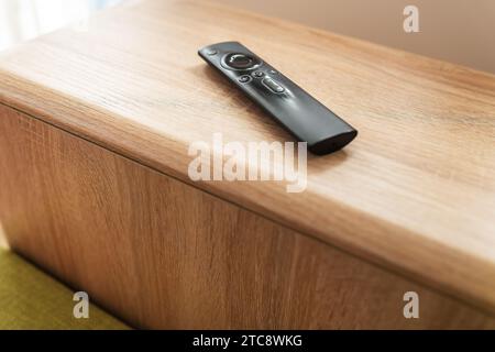 A black remote control on a wooden surface. The remote is in focus and the background is blurred Stock Photo