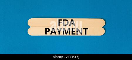 FDA Food and Drug Administration payment symbol. Concept words FDA payment on beautiful wooden stick. Beautiful blue table blue background. Business F Stock Photo