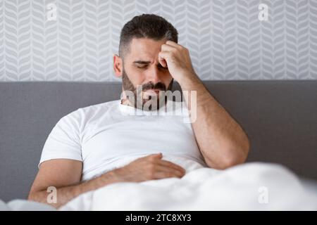Unhappy man lying in bed touching head having migraine indoor Stock Photo