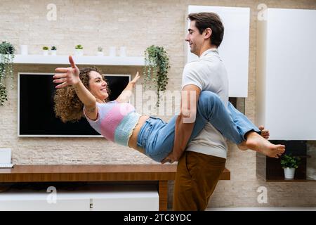 Joyful couple embracing against TV and potted plants at home Stock Photo