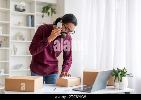 Indian Man Talking On Cellphone And Checking Packed Boxes With Orders Stock Photo