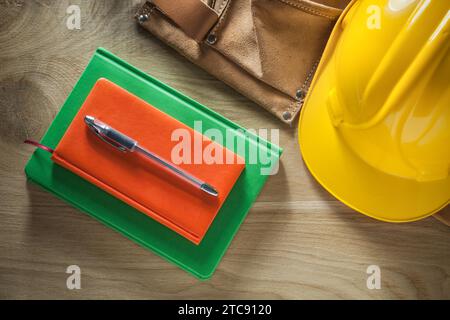 Notebooks Pen Leather tool belt Hard hat on wooden board Stock Photo
