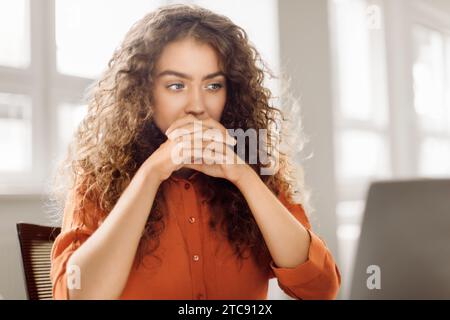 Curly-haired woman deep in thought at computer Stock Photo