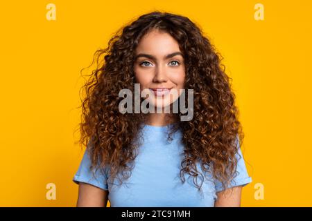 Confident curly-haired woman smiling on yellow Stock Photo