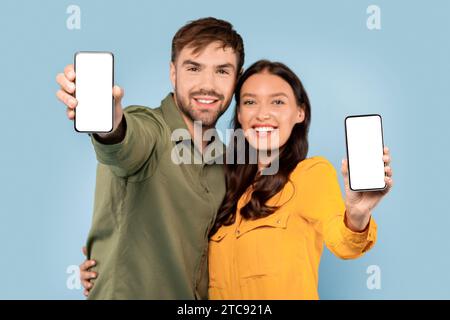Smiling couple showing smartphones with blank screens on blue Stock Photo