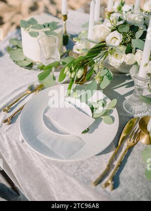 Elegant table setting with a paper card decorated with eucalyptus branches close up. Romantic table with paper invitation card. Wedding Mockup. Stock Photo
