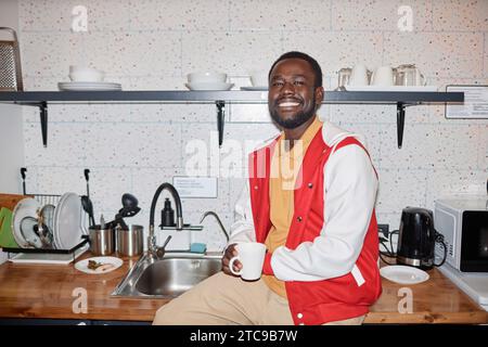 Waist up portrait of smiling Black man wearing varsity jacket smiling at camera in kitchen, with flash Stock Photo