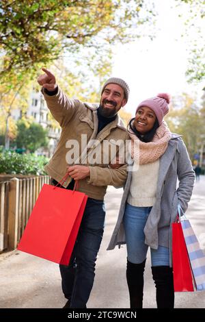 Multiracial couple walking in the city doing christmas shoppings together, pointing at things. Stock Photo