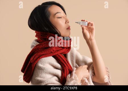 Ill Asian woman with nasal drops on beige background, closeup Stock Photo