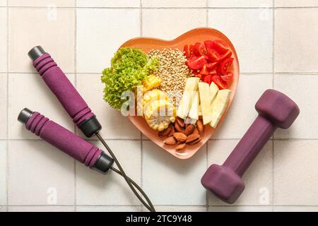 Plate with fresh healthy products, dumbbell and jumping rope on light tile background. Diet concept Stock Photo