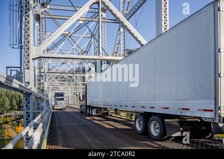 Long hauler two industrial big rig semi trucks with loaded semi trailers moving towards each other they met on a narrow truss bridge having difficulty Stock Photo