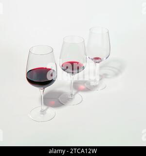 Three glasses with lowering levels of red wine poured, isolated on white. Concept of mindful drinking and alcohol cutback. Stock Photo