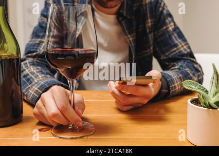 Unrecognizable man holding a phone and a glass of wine, tracking amount of alcohol with an app or rating a wine, close-up view Stock Photo