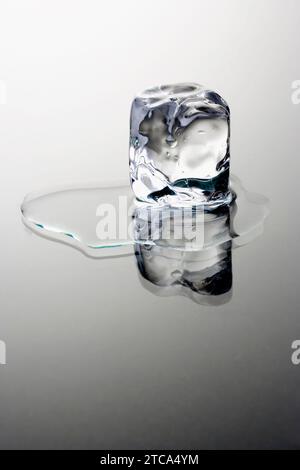 Melting Ice Cube on grey background with reflection Stock Photo