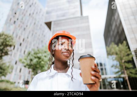 Happy black woman in helmet standing with coffee cup in daylight Stock Photo