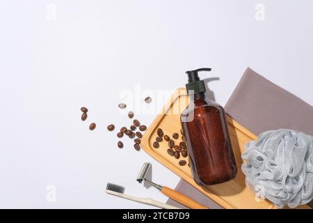 A brown shampoo bottle is displayed on a wooden tray with coffee beans on a white background. Empty space for text design. View from above, copy space Stock Photo