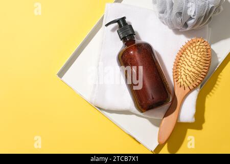 Close-up of a brown shampoo bottle, a detangling comb, a towel and a bath sponge placed on a tray against a yellow background. Copy space for ads. Stock Photo