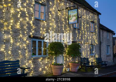 Christmas lights on The Swan pub at dusk. Southrop. Cotswolds, Gloucestershire, England Stock Photo