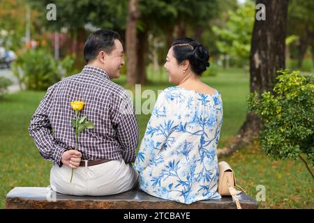 Senior man hiding flower behind back as a romantic surprise for girlfriend Stock Photo