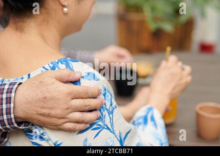 Senior man hugging his wife when they are having coffee in coffeeshop Stock Photo