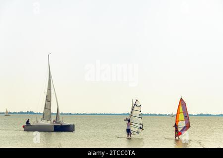 Podersdorf am see, Austria, August 15 2015: Catamaran boat and two windsurfers on neusiedler lake in cloudy summer day Stock Photo