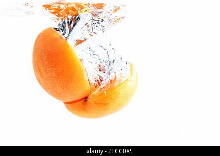 Fresh apricot spitted in half falling in water splash. Half of fruit in water with air blister. Isolated on white background Stock Photo