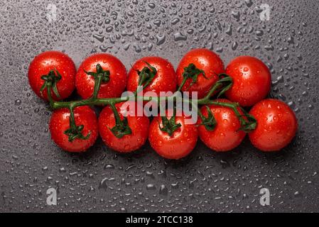 Red cherry tomatoes on a vine isolated on a black wet background. Warer drops on black Stock Photo