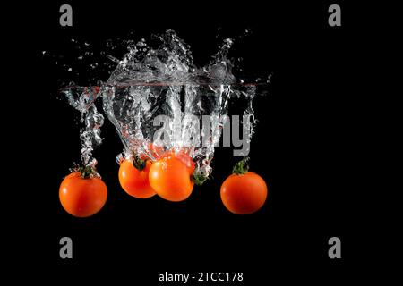 Cherry tomatoes isolated on black wet background falling into water with splash. Copy space Stock Photo