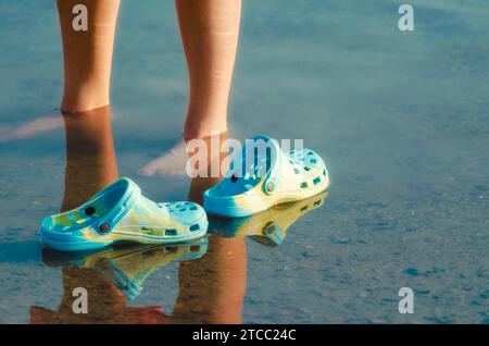 Rubber slippers float in clear water next to female legs closeup Stock Photo