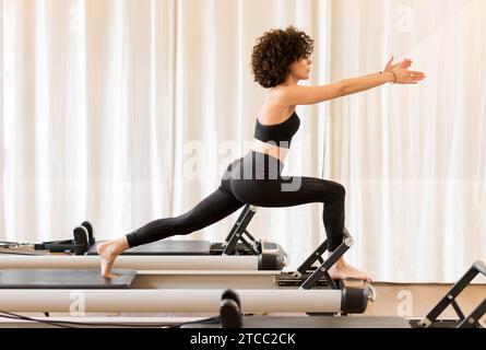 Woman in black workout clothes adjusting reformer bed in a pilates