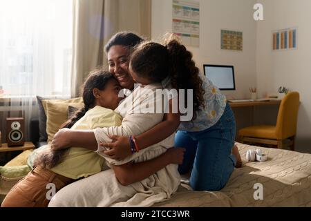 Daughters embracing their happy mother while spending time together at home Stock Photo