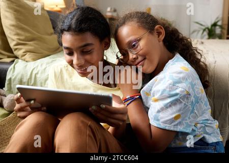 Two sisters sitting in their room and using tablet pc together, they watching funny video Stock Photo