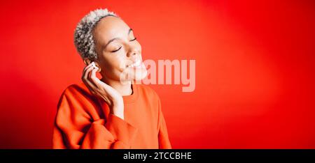 Happy young woman dancing while wearing wireless earphones in a studio. Woman listening her favourite music playlists. Stock Photo