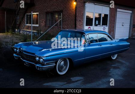 American classic car, blue Cadillac in front of red brick building, industrial area, night shot, Raettvik, Dalarna, Sweden Stock Photo