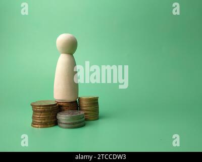 Wooden people figures and coins on a green background with copy space. Stock Photo