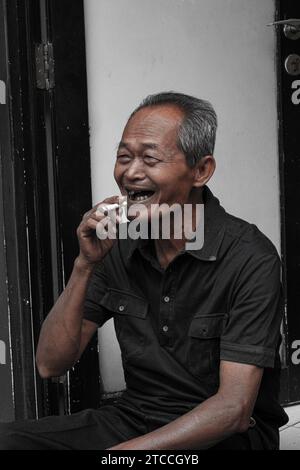 an asian man sitting on the ground and smiling in the streets of Kemang Stock Photo