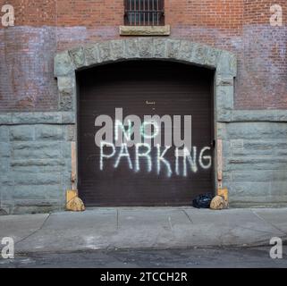 A close-up of a brick building garage door with a no parking spray paint message in white letters Stock Photo