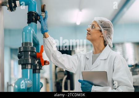 Drinking water factory purification process. Hygiene factory worker female monitor checking valve and water pipe production flow control. Stock Photo