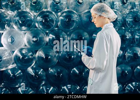 women worker working in drinking water plant factory checking count water bottle gallon in warehouse with hygiene uniform. Stock Photo