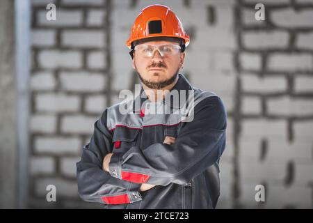 Portrait of a serious bearded Caucasian worker in overalls, safety helmet and safety glasses at a construction site Stock Photo