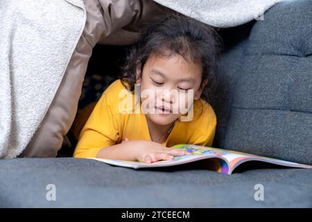 A girl is sitting on the sofa at home, reading a book Stock Photo
