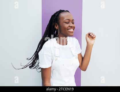 Young smiling female enjoying a good mood. Happy woman in white overalls standing at the wall. Stock Photo