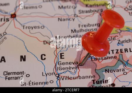 A red pin stuck into a map of Western Europe, pinpointing the location of Geneva Stock Photo