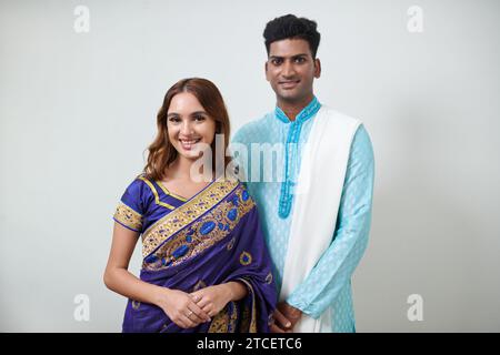 Portrait of happy Indian man and woman in traditional clothes standing against white wall Stock Photo