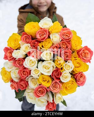 large bouquet of many multi-colored roses in the hands of a boy out of focus on a light snowy background. Mothers Day. International Women's Day. Vale Stock Photo