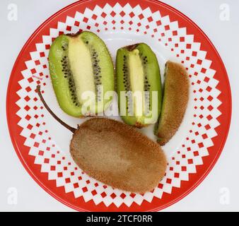 Kiwifruit Actinidia deliciosa 'Hayward' fruit whole and sliced on a red and white patterned plate top down view Stock Photo