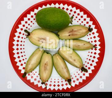 White guava fruit Psidium guajava whole and sliced on a red and white patterned plate top down view Stock Photo