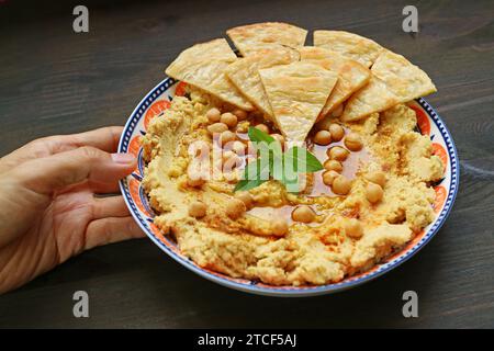 Hand Placing Freshly Made Hummus with Pita Bread on Wooden Table Stock Photo